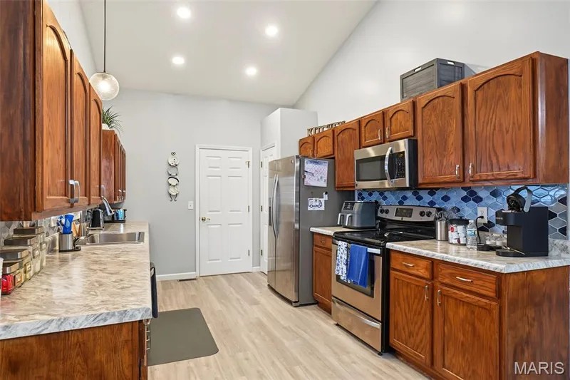 Vaulted ceiling featuring recessed lighting, extensive wood cabinetry, wood-finish flooring, and stainless steel appliances — 8 Soenker Circle, St Peters, MO 63376