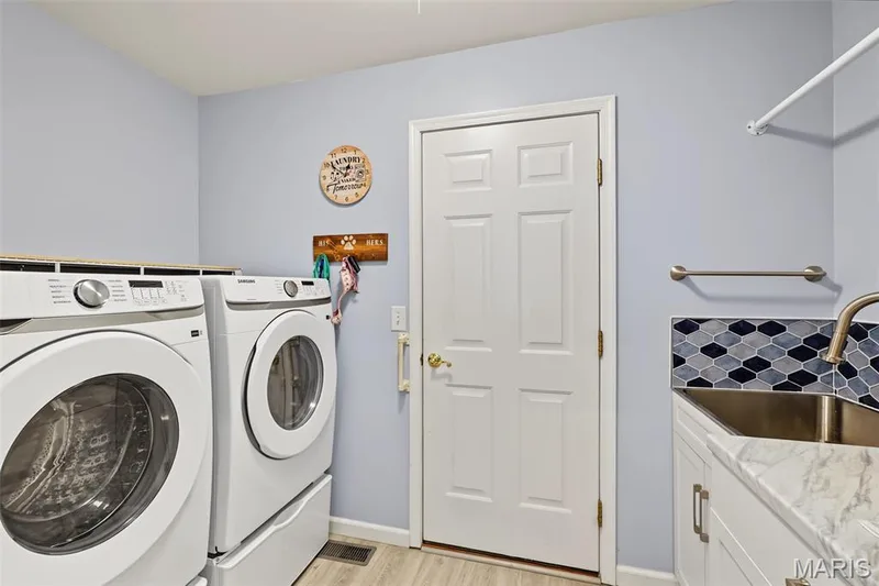Laundry area with wood-finish flooring, a utility sink with a gooseneck faucet, and a patterned tile backsplash — 8 Soenker Circle, St Peters, MO 63376