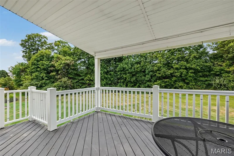 Covered deck with a dark-finished floor, white railings, and a verdant backdrop — 8 Soenker Circle, St Peters, MO 63376