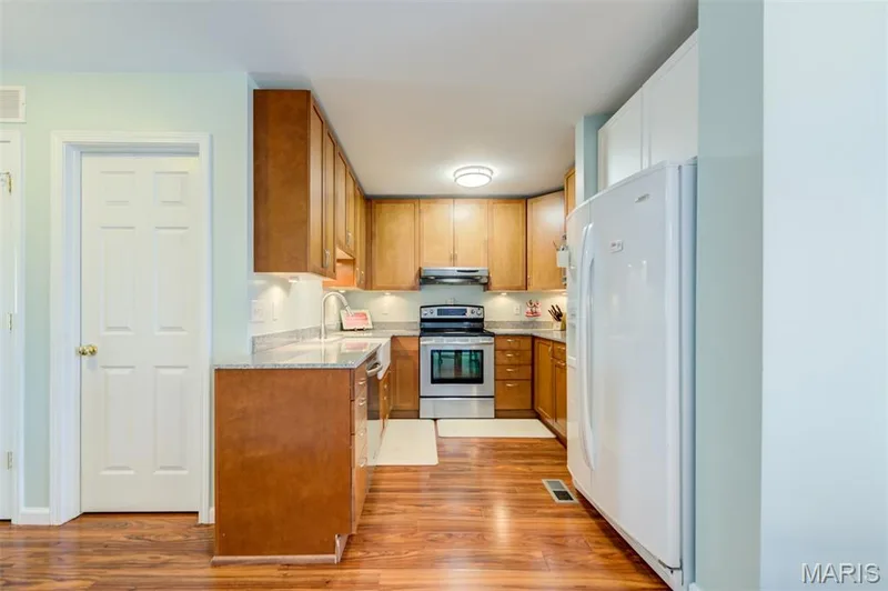 Kitchen featuring wood-finish flooring, wood cabinetry, stone countertops, and stainless steel appliances — 820 Brookmead Drive, O'Fallon, MO 63366