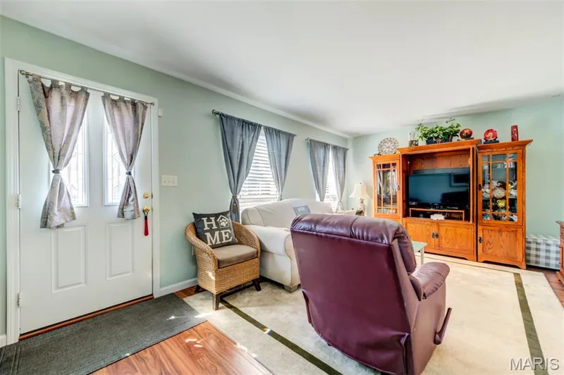 Wood-finish flooring with a light-toned area rug, white trim, light-colored walls, and a front entry door with decorative glass inserts — 820 Brookmead Drive, O'Fallon, MO 63366