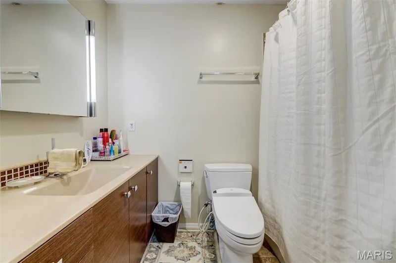 Bathroom featuring an integrated countertop sink, wood-finish cabinetry, a large vanity mirror with integrated lighting, and a white toilet — 820 Brookmead Drive, O'Fallon, MO 63366