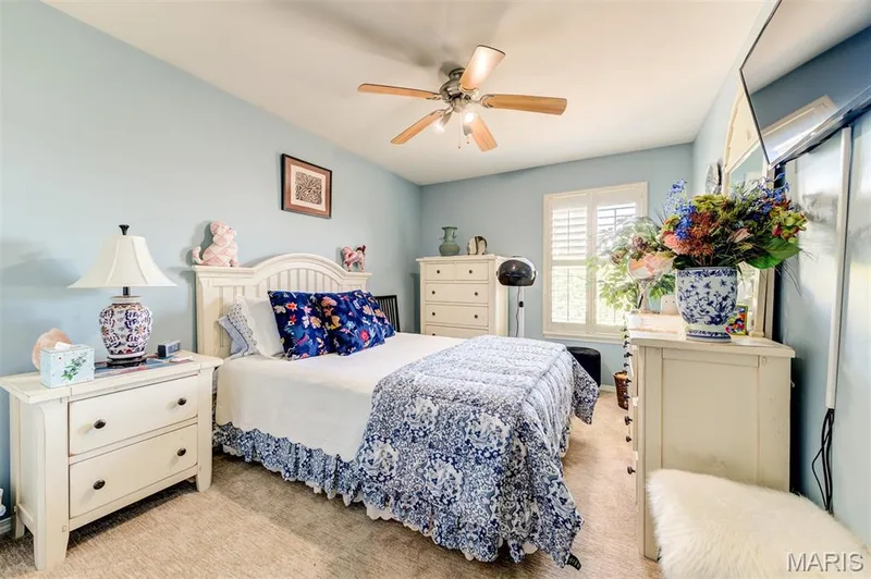 Sloped ceiling with ceiling fan, window with white plantation shutters, wood-finish flooring, and white paneled headboard — 820 Brookmead Drive, O'Fallon, MO 63366
