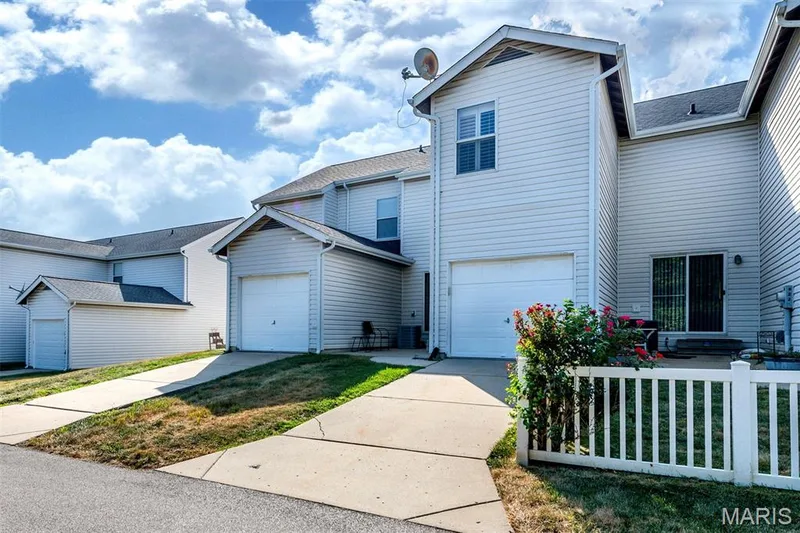 Vinyl siding exterior with an attached garage, paved driveway, and a white picket fence — 820 Brookmead Drive, O'Fallon, MO 63366
