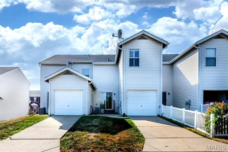 White vinyl siding exterior with two attached garages, individual paved driveways, a rear patio with a glass sliding door, and a white picket fence — 820 Brookmead Drive, O'Fallon, MO 63366