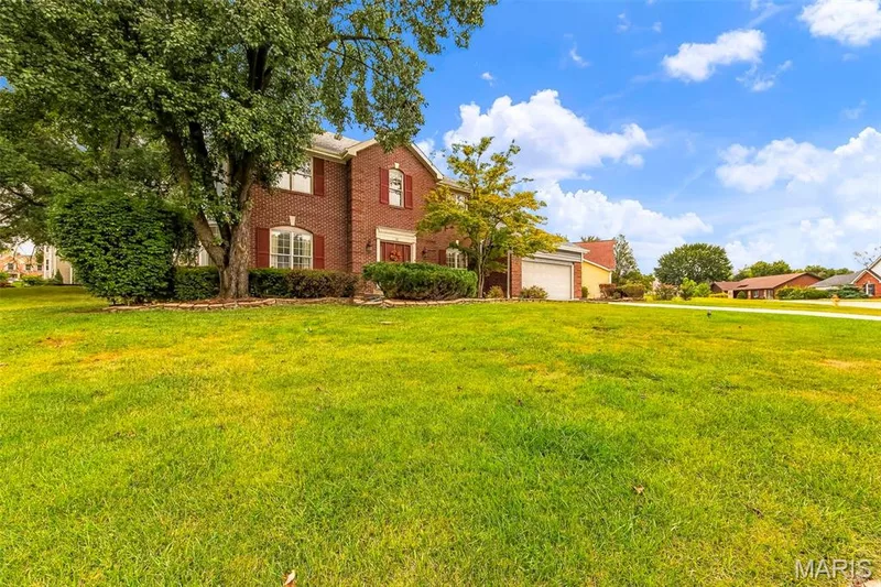 Brick exterior with white window frames and red shutters, mature trees, manicured shrubs, and an attached garage — 11 Silver Leaf Court, Lake St. Louis, MO 63367