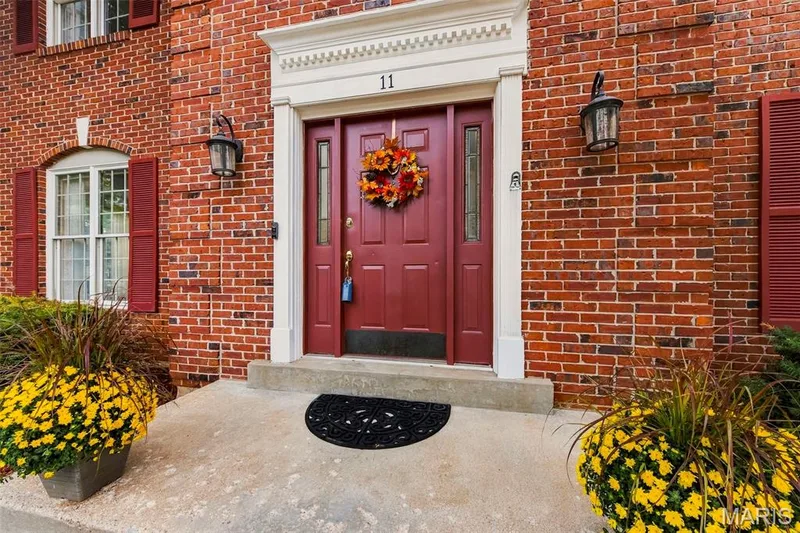 Red brick exterior with white trim, a red paneled front door, and two wall-mounted exterior light fixtures — 11 Silver Leaf Court, Lake St. Louis, MO 63367
