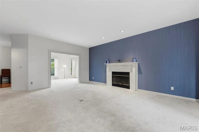 Expansive carpeted room featuring a white mantel fireplace with a dark surround, recessed lighting, and a textured accent wall — 11 Silver Leaf Court, Lake St. Louis, MO 63367