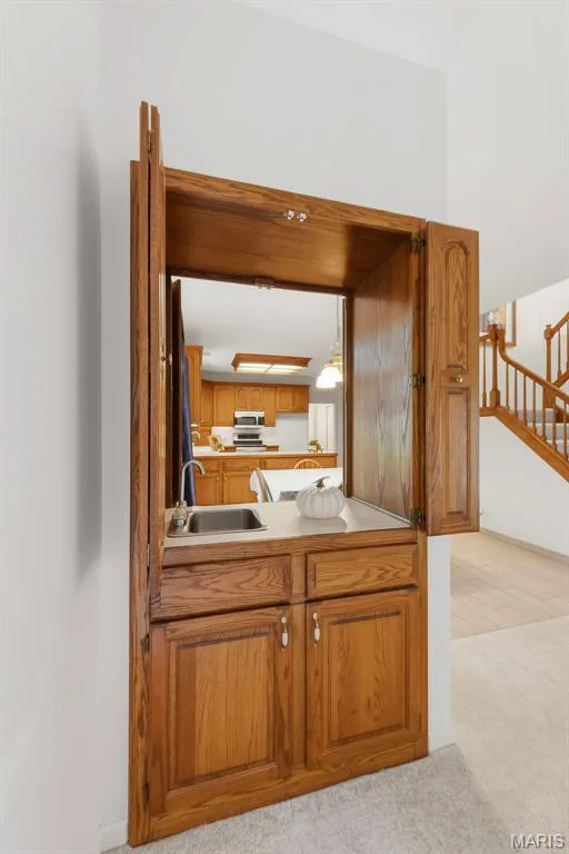 Built-in wood-finish cabinetry featuring a stainless steel sink, countertop, and storage with paneled doors — 11 Silver Leaf Court, Lake St. Louis, MO 63367