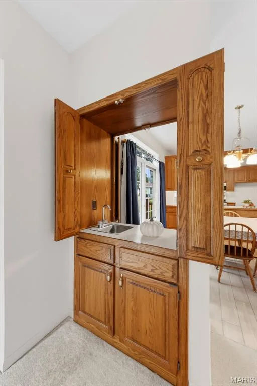 Built-in wet bar featuring a stainless steel sink, chrome faucet, white countertop, and wood-finish cabinetry — 11 Silver Leaf Court, Lake St. Louis, MO 63367
