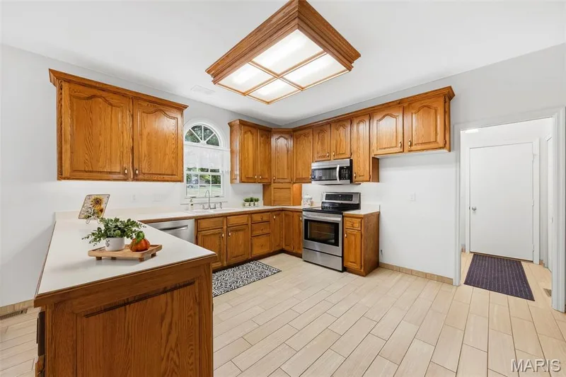 Oak cabinetry with white countertops, stainless steel appliances, and a tiled floor — 11 Silver Leaf Court, Lake St. Louis, MO 63367