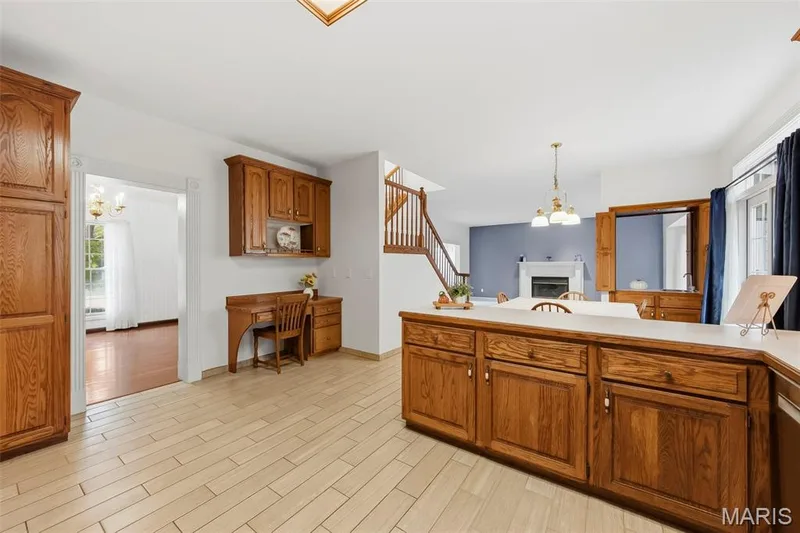 Warm wood cabinetry with a light countertop, light tile flooring, and integrated built-in desk — 11 Silver Leaf Court, Lake St. Louis, MO 63367