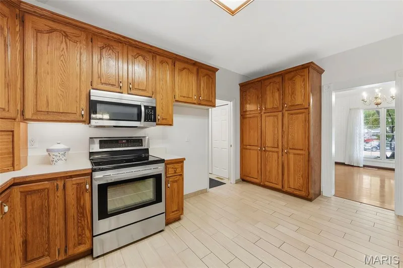 Kitchen featuring extensive wood cabinetry, stainless steel oven with cooktop, built-in microwave, light-toned tile flooring, and a white countertop — 11 Silver Leaf Court, Lake St. Louis, MO 63367