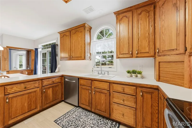Wood-finish cabinetry with white countertops, stainless steel dishwasher, and a double-basin sink — 11 Silver Leaf Court, Lake St. Louis, MO 63367