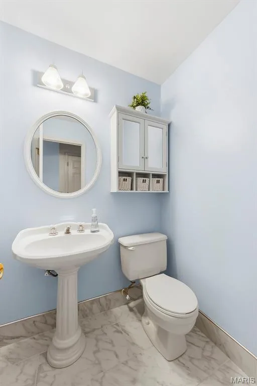 Half bath Pedestal sink, wall-mounted storage cabinet, round mirror, and marble-finish tile flooring — 11 Silver Leaf Court, Lake St. Louis, MO 63367