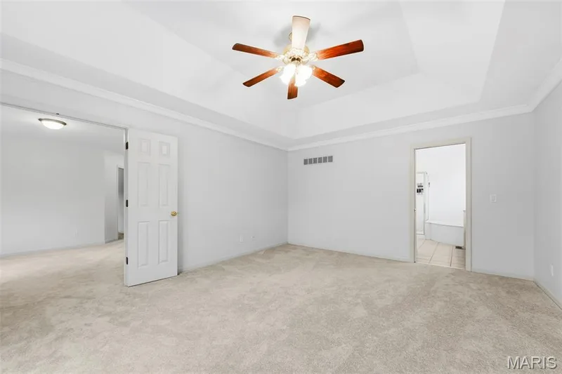 Tray ceiling with crown molding, ceiling fan, and light-toned wall-to-wall carpeting — 11 Silver Leaf Court, Lake St. Louis, MO 63367