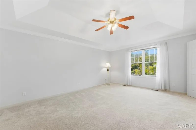 Tray ceiling with crown molding, ceiling fan light fixture, large window, and light-toned carpet — 11 Silver Leaf Court, Lake St. Louis, MO 63367