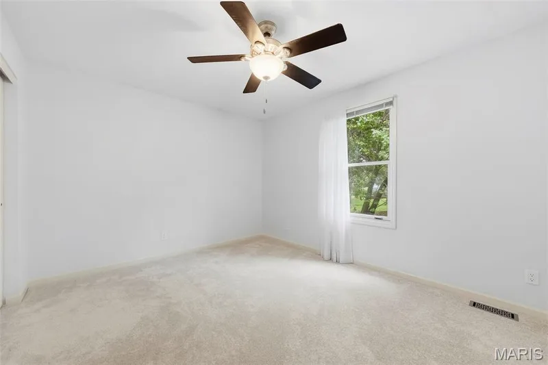 Neutral carpet flooring, white painted walls, ceiling fan with integrated lighting, and a window with white trim — 11 Silver Leaf Court, Lake St. Louis, MO 63367