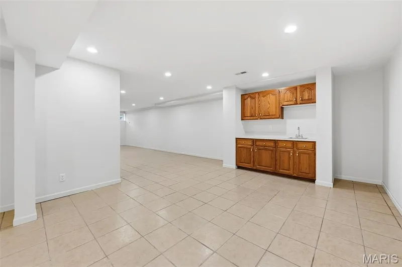 Spacious room featuring tile flooring, recessed lighting, and a built-in wet bar with wood cabinetry and a stainless steel sink — 11 Silver Leaf Court, Lake St. Louis, MO 63367