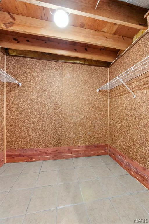 Exposed ceiling joists with a single light fixture, textured wall panels, cedar wood baseboard, and tiled flooring — 11 Silver Leaf Court, Lake St. Louis, MO 63367