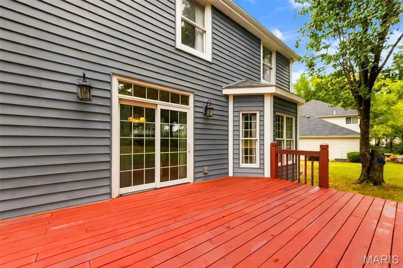 Expansive wood-finish deck with red stain, featuring sliding glass doors and an exterior wall lantern — 11 Silver Leaf Court, Lake St. Louis, MO 63367