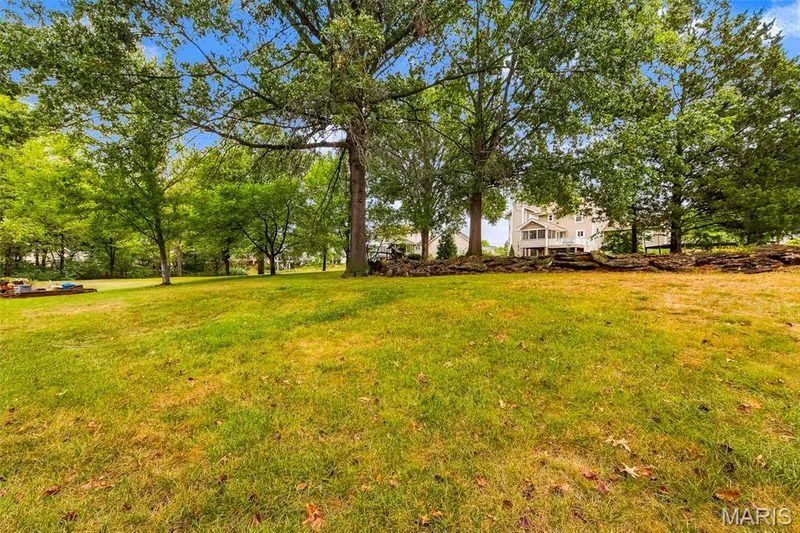 Expansive green lawn with mature trees and a stone retaining wall — 11 Silver Leaf Court, Lake St. Louis, MO 63367