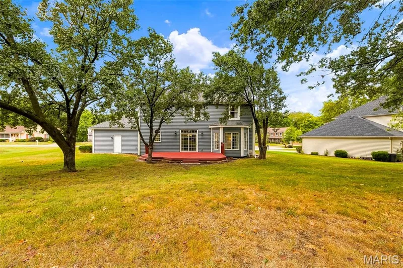 Expansive lawn with mature trees, a multi-level deck, bay window, and light-colored siding — 11 Silver Leaf Court, Lake St. Louis, MO 63367