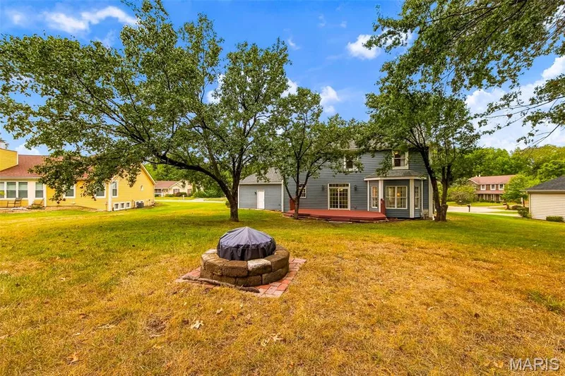 Expansive backyard featuring a brick paver fire pit, mature trees, and a spacious rear deck — 11 Silver Leaf Court, Lake St. Louis, MO 63367