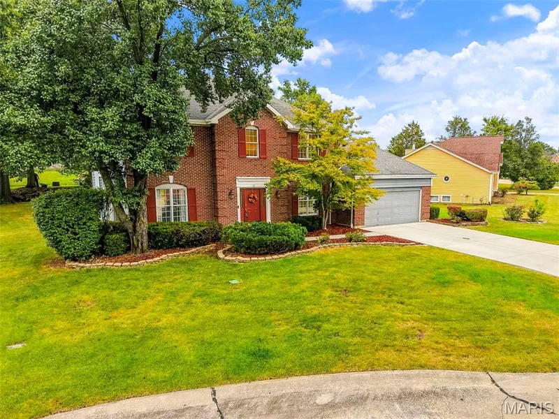 Brick exterior with red shutters, attached two-car garage, concrete driveway, and mature landscaping — 11 Silver Leaf Court, Lake St. Louis, MO 63367