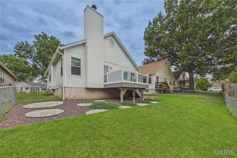 Rear exterior featuring a large elevated composite  deck, a prominent chimney, and a landscaped area with decorative stone — 2931 Plum Leaf Circle, St Peters, MO 63303