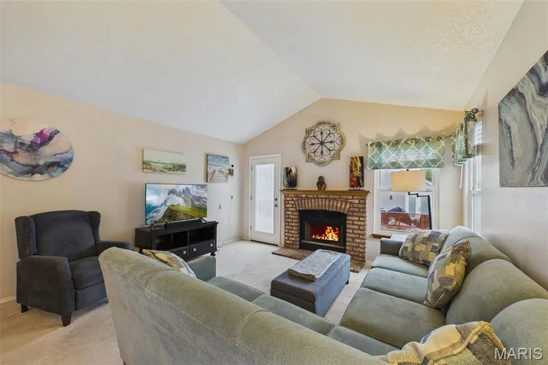 Vaulted ceiling living area featuring a brick-surround fireplace, multiple windows with exterior visibility, and a glass-paneled door — 2931 Plum Leaf Circle, St Peters, MO 63303