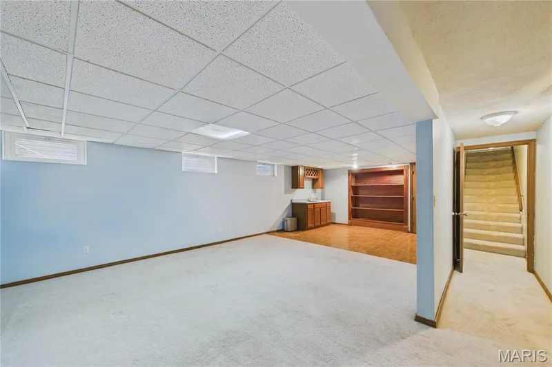 Finished lower level featuring a drop ceiling, built-in shelving, finished flooring, and a compact wet bar with wood cabinetry — 2931 Plum Leaf Circle, St Peters, MO 63303