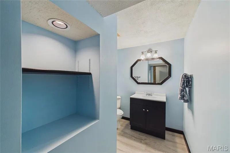 Bathroom w/Built-in shelving & recessed lighting, dark wood-finish vanity, white countertop with integrated sink, and an octagonal framed mirror — 2931 Plum Leaf Circle, St Peters, MO 63303