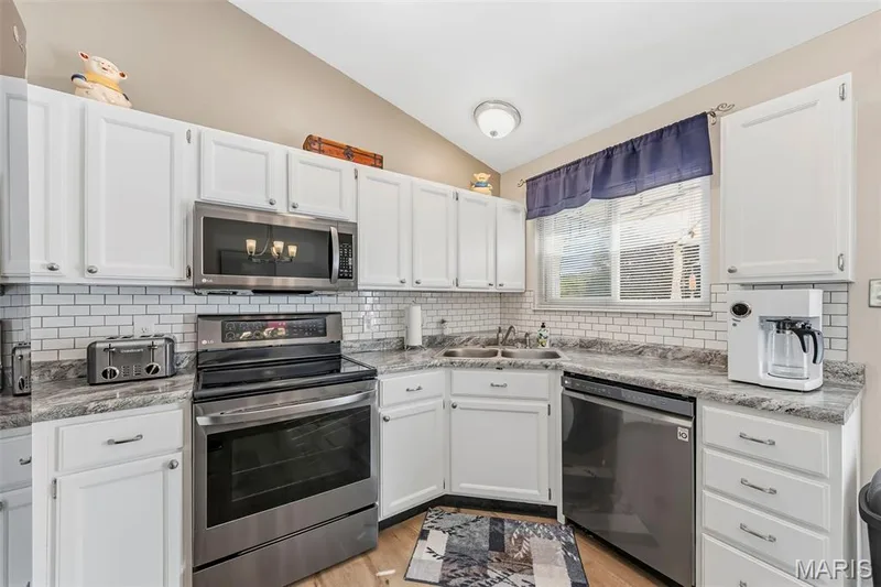 Kitchen featuring white cabinetry, subway tile backsplash, stainless steel appliances, and wood-finish flooring — 202 Kunze Drive, St Charles, MO 63303