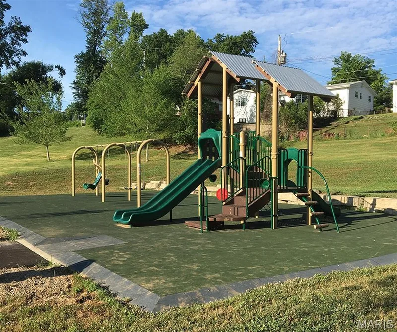 Playground area featuring a multi-level structure with slides and swings, set on a dark green padded surface — 202 Kunze Drive, St Charles, MO 63303