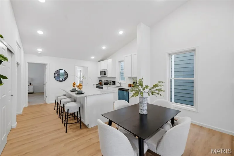 Open-concept living space with vaulted ceilings, LVP flooring, a kitchen island with granite countertop, and contemporary kitchen cabinetry — 9023 Wilkie Station Street, St Charles, MO 63301