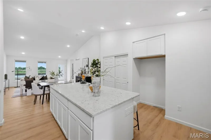 Open-concept living space featuring LVP flooring, a kitchen island with granite countertop, white cabinetry, and recessed lighting — 9023 Wilkie Station Street, St Charles, MO 63301