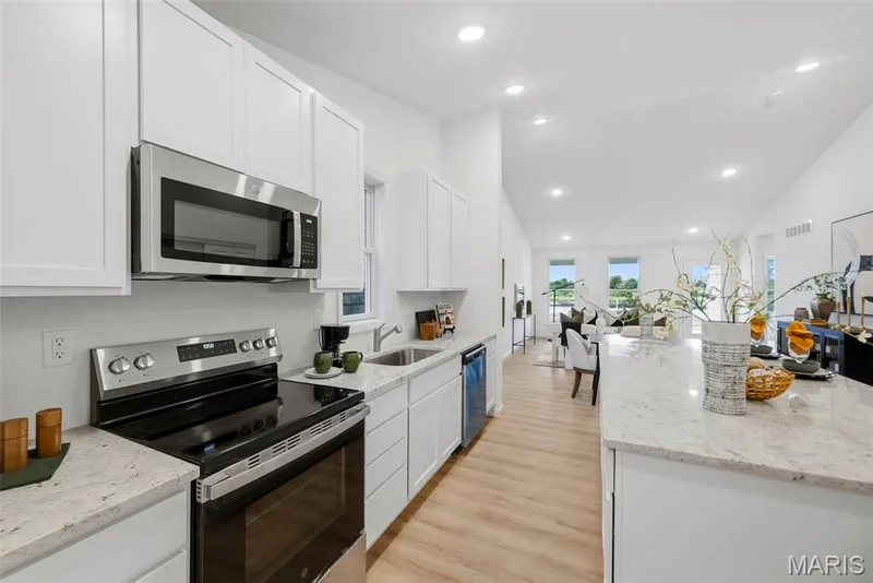 Open-concept kitchen featuring white cabinetry, stainless steel appliances, granite countertops & LVP flooring — 9023 Wilkie Station Street, St Charles, MO 63301