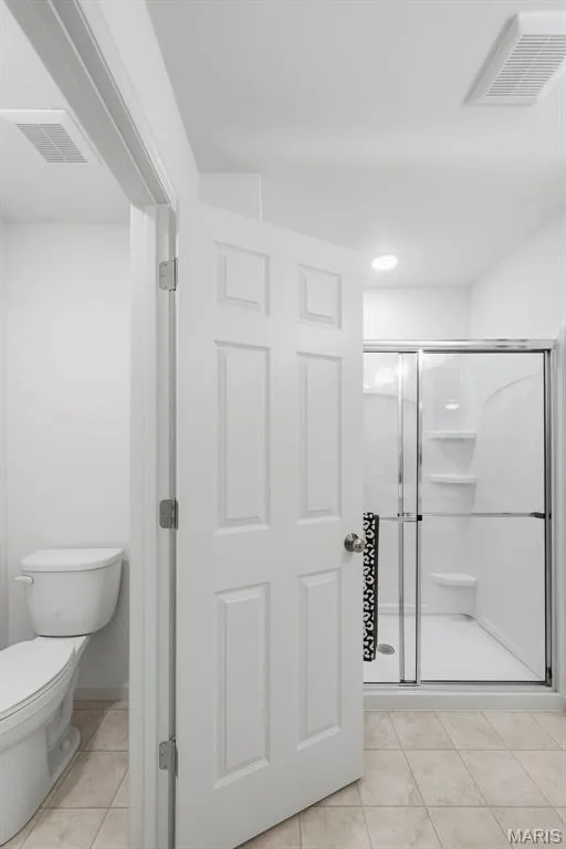 White paneled door opening to a bathroom with a toilet, and a glass-enclosed shower with built-in shelving — 9023 Wilkie Station Street, St Charles, MO 63301