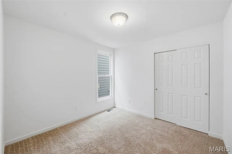 Neutral color palette with textured carpeting, a window with horizontal blinds, and a closet with sliding panel doors — 9023 Wilkie Station Street, St Charles, MO 63301