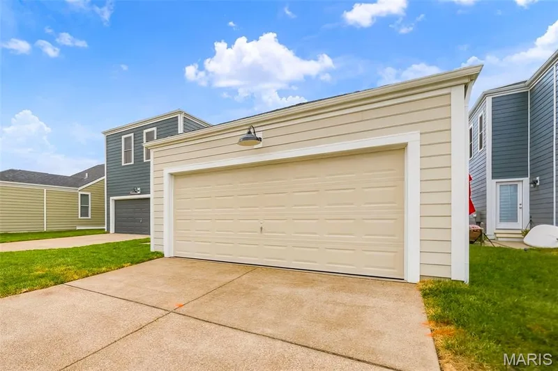 Attached garage with a beige panel door and an overhead industrial-style light fixture — 9023 Wilkie Station Street, St Charles, MO 63301