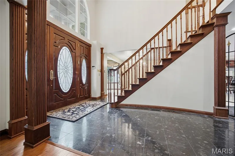 Grand entryway featuring a double-height ceiling, large leaded glass double entry doors, wood-finish columns, and a wide staircase with wood-finish railings — 76 River Valley Drive, Chesterfield, MO 63017