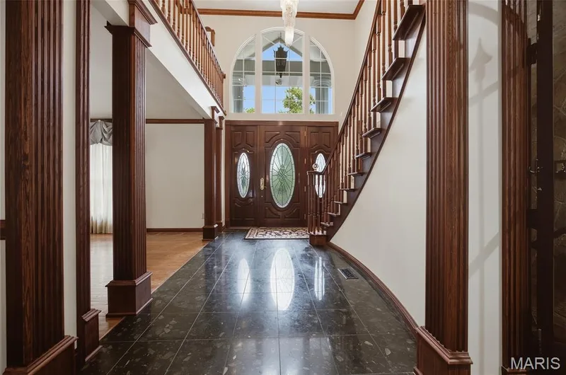 Two-story foyer featuring dark wood-finish columns and banister, a curved staircase, a wood-finish double entry door with oval glass inserts, and a large arched transom window — 76 River Valley Drive, Chesterfield, MO 63017