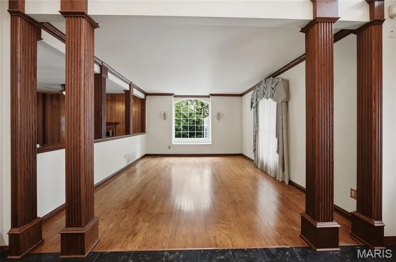 Hardwood flooring with dark wood trim, fluted wood columns, and a large arched window with wall sconces — 76 River Valley Drive, Chesterfield, MO 63017