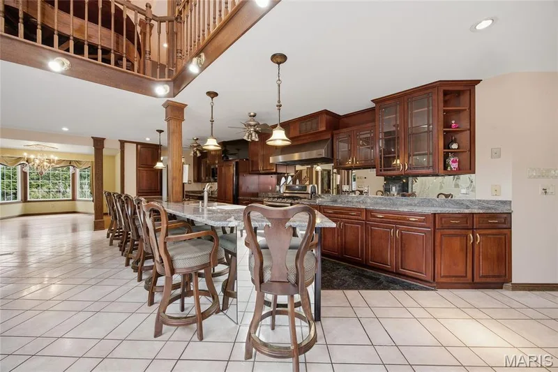 Open-concept kitchen featuring extensive wood cabinetry, granite countertops, and a large island with pendant lighting — 76 River Valley Drive, Chesterfield, MO 63017