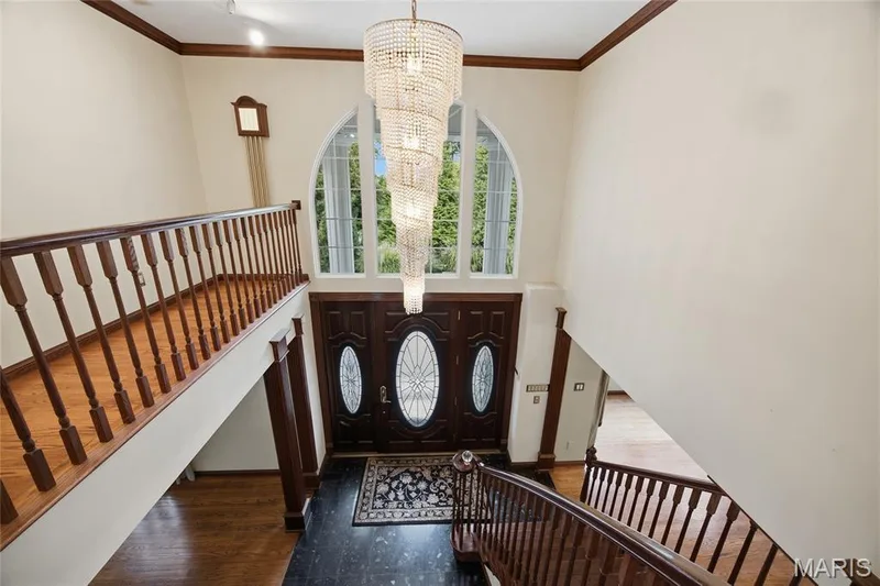 Two-story foyer with a grand chandelier, arched window, double entry doors with oval glass inserts, dark wood flooring, and curved staircase — 76 River Valley Drive, Chesterfield, MO 63017