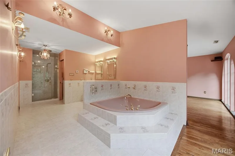 Corner soaking tub with tiled surround, walk-in shower with glass enclosure, dual vanity mirrors with integrated lighting, and tile flooring. Workout room or possible nursery space behind this space. — 76 River Valley Drive, Chesterfield, MO 63017