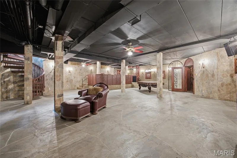 Spacious lower-level area featuring stone-finish walls, exposed ceiling beams, and a wood spiral staircase — 76 River Valley Drive, Chesterfield, MO 63017