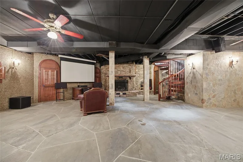 Irregular flagstone flooring, stone accent walls, spiral wood-finish staircase, built-in fireplace, and a ceiling-mounted fan — 76 River Valley Drive, Chesterfield, MO 63017