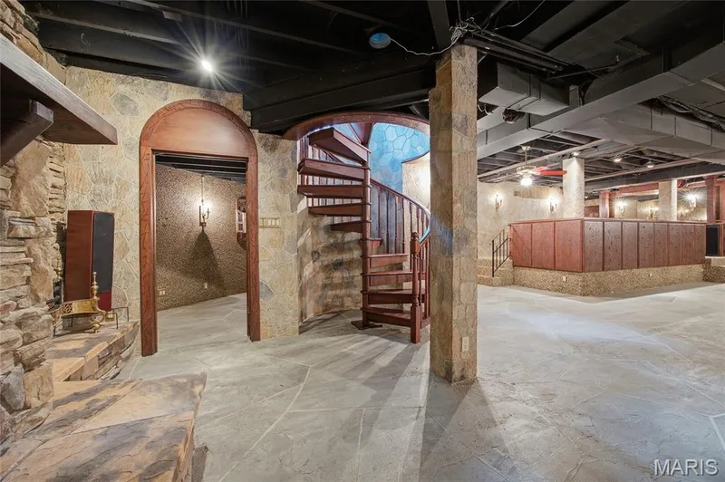 Stone flooring with accent stone wall, arched wood-finish doorway, and wood-finish spiral staircase — 76 River Valley Drive, Chesterfield, MO 63017